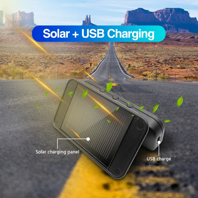 A black solar charging panel device is shown on an asphalt road, demonstrating solar and USB charging capabilities.