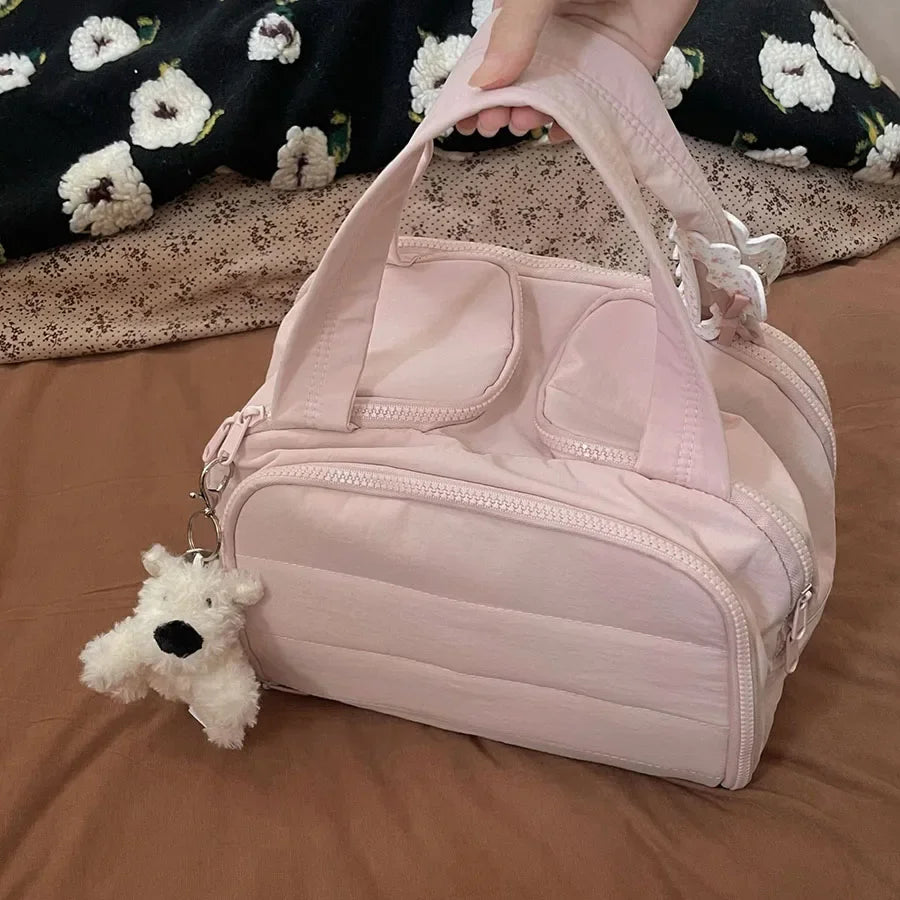 A pink cosmetic travel organizer bag with a white bear charm resting on brown fabric.