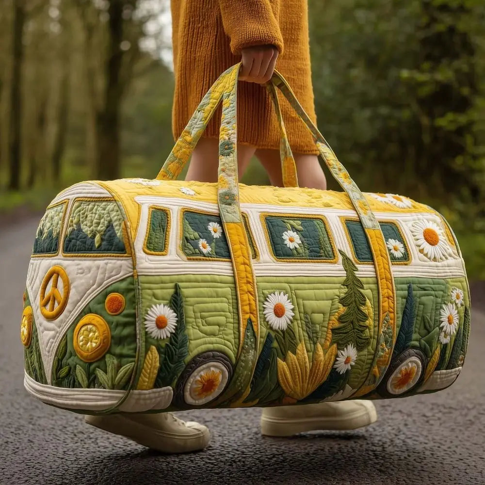 A yellow quilted travel duffle bag with green and white floral stitching is being held by a person in a forest setting.