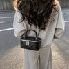 A woman is holding a black woven PU leather crossbody bag with a silver chain against a gray background.