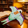 A plush toy resembling a luna moth with green and purple wings resting on a wooden surface.