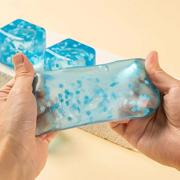 Une main tient une boule anti-stress de flocon bleu translucide à côté de deux morceaux plus grands en forme de glaçons.