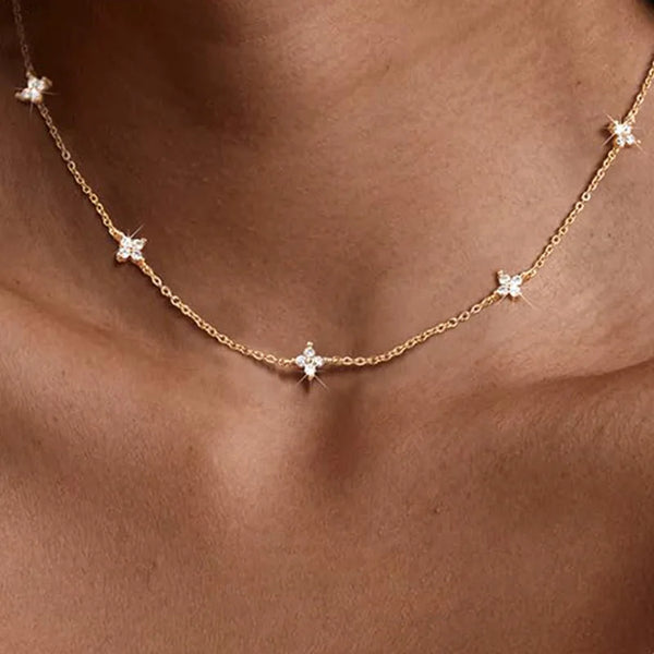 A close-up of a dainty gold necklace featuring small white CZ flowers and leaves worn around the neck.