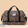 Braun-schwarze Leopardenmuster-Gepäcktasche mit schwarzen Riemen auf hellem Beige.