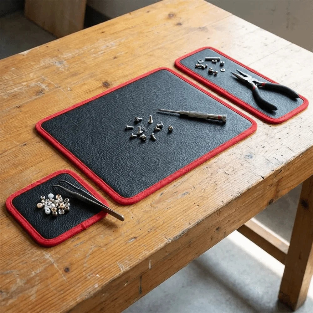 A black tool mat with a red border is placed on a wooden table, showing various metal tools and pliers.