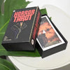 A black box of the Horror Tarot card deck is displayed next to a green leaf on a white surface.