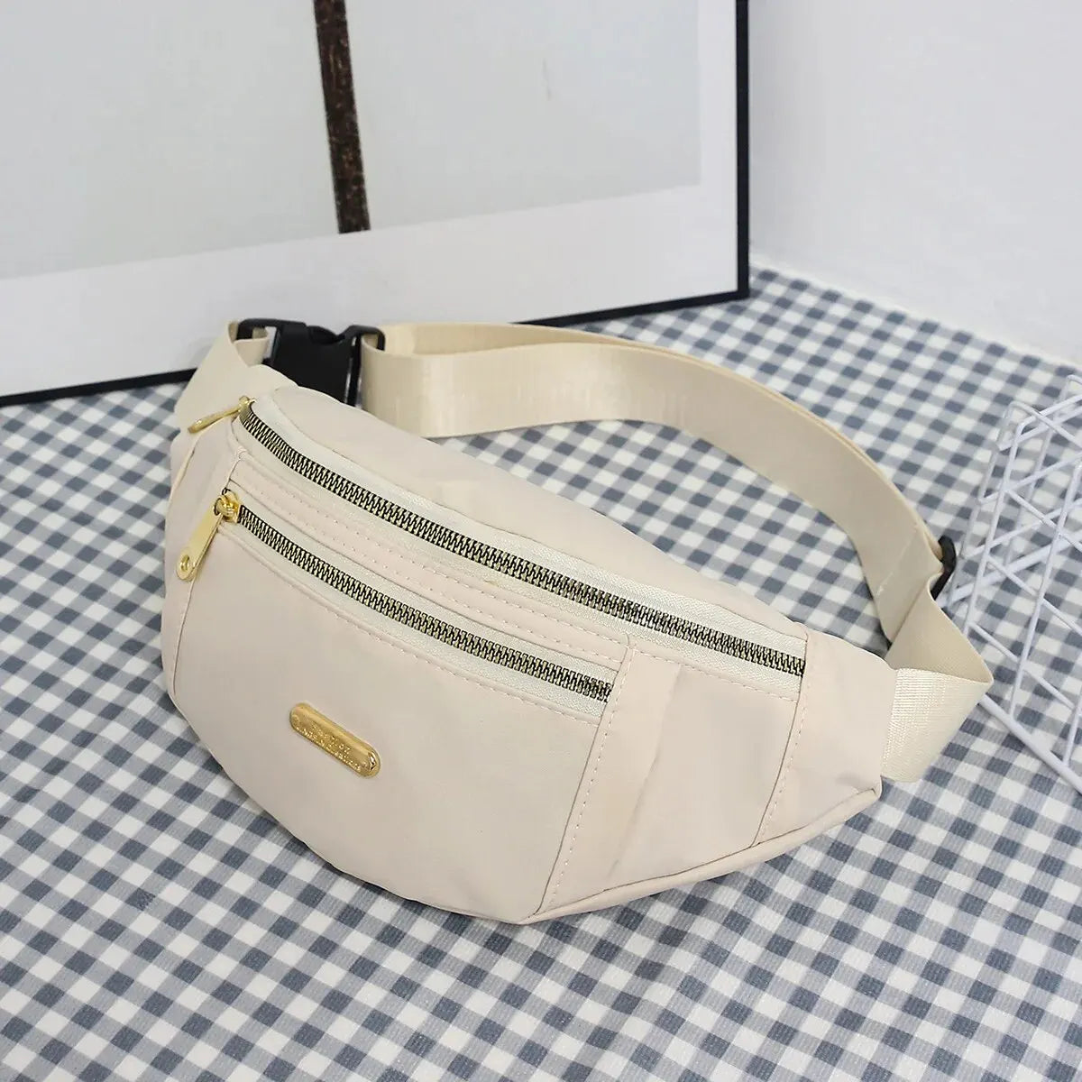 Beige Damen-Sport-Fanny-Pack mit Reißverschluss und Lederriemen auf kariertem Untergrund.
