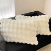 A white, fluffy quilted pillowcase is displayed on a dark surface.