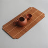 A terracotta teapot rests on a bamboo tea mat with visible stitching.