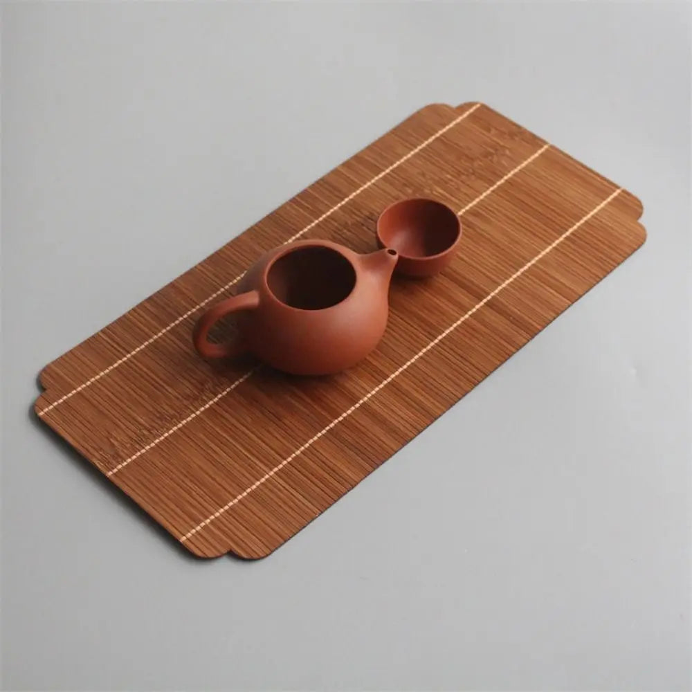 A terracotta teapot rests on a bamboo tea mat with visible stitching.