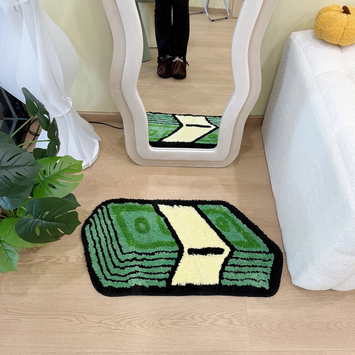 A green and yellow cartoon dollar bill mat with a textured border is placed on a light wood floor in front of a mirror.