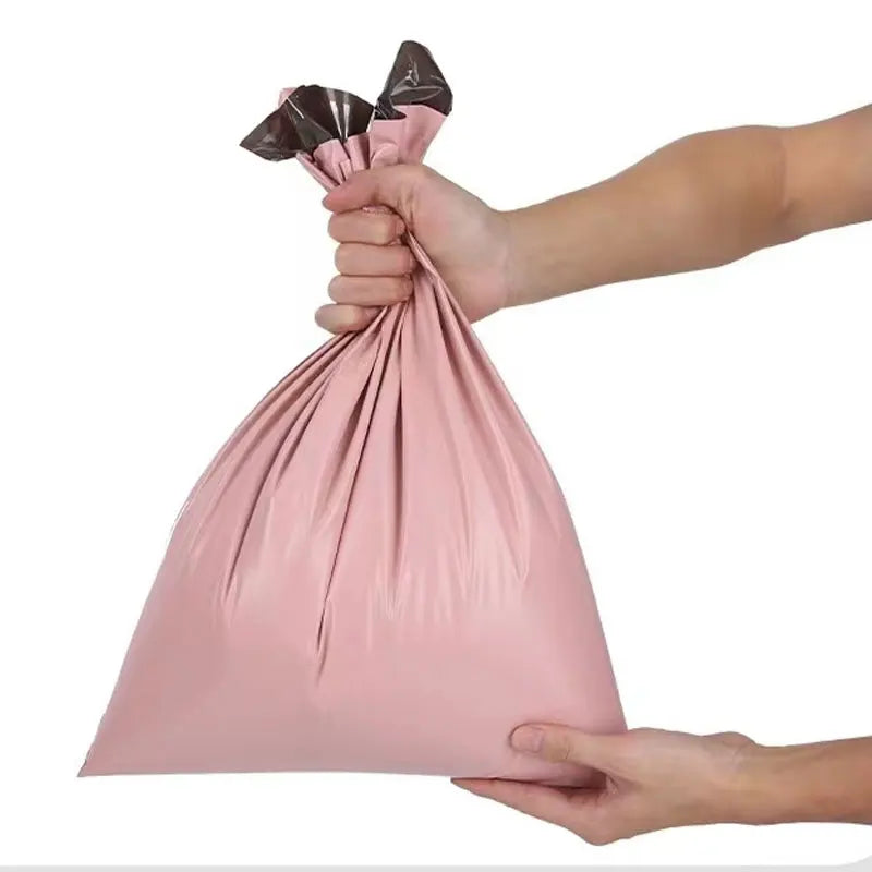 A hand is holding a pink waterproof poly mailer shipping bag with a black ribbon tied at the top.