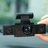 A hand holds a black dash cam with a wide-angle lens, positioned for recording.
