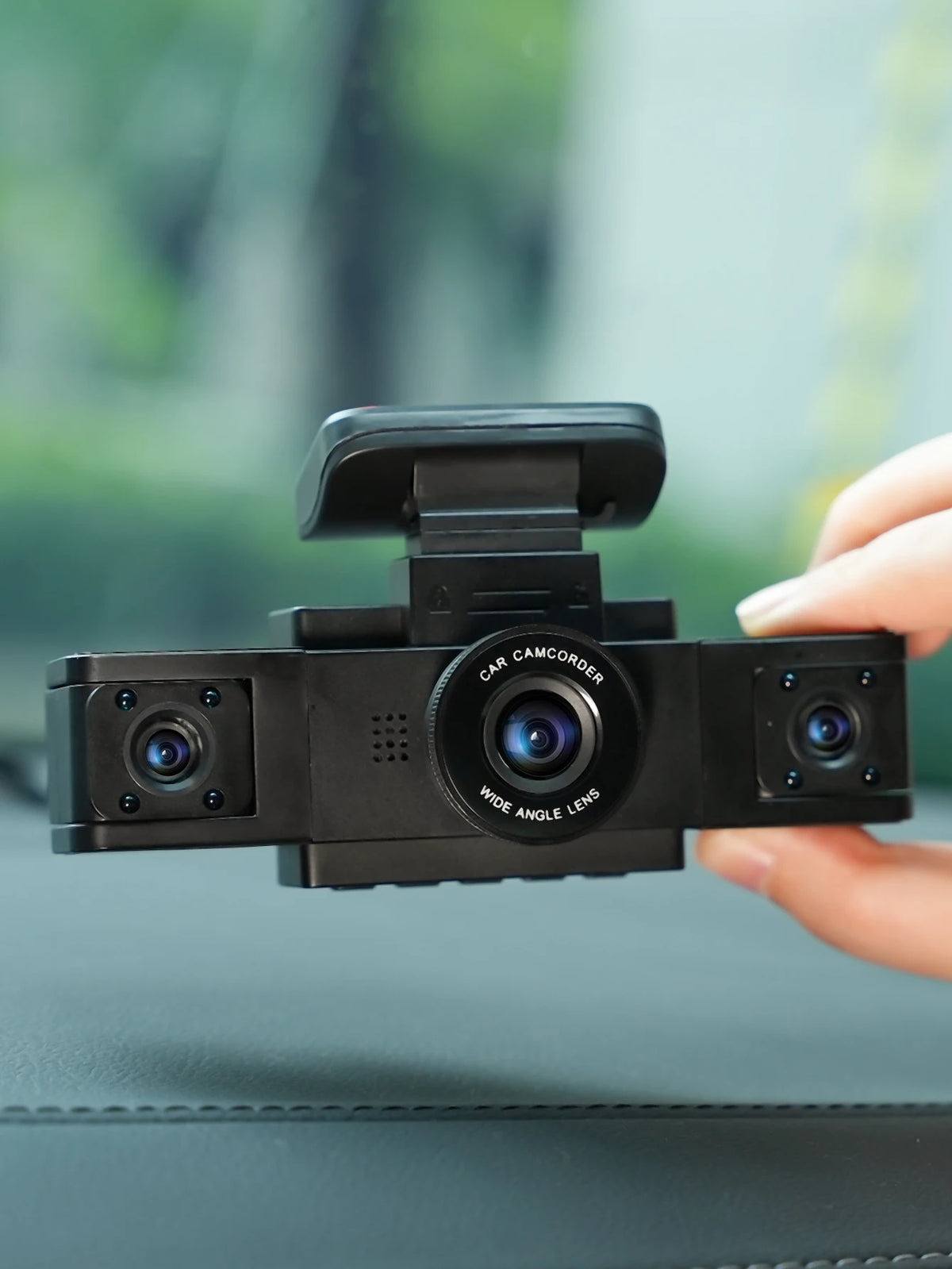 A hand holds a black dash cam with a wide-angle lens, positioned for recording.