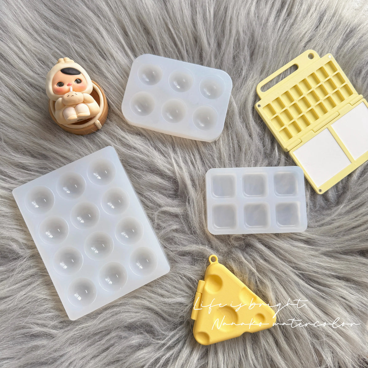 A collection of silicone paint palette trays in white and yellow are displayed on a fluffy gray surface.