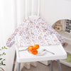 A white table displays a long-sleeve waterproof baby bib with a cute animal design featuring brown and purple patterns.