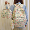 A person is wearing a light blue shirt and beige pants while holding a floral patterned backpack, handbag, and pencil case.