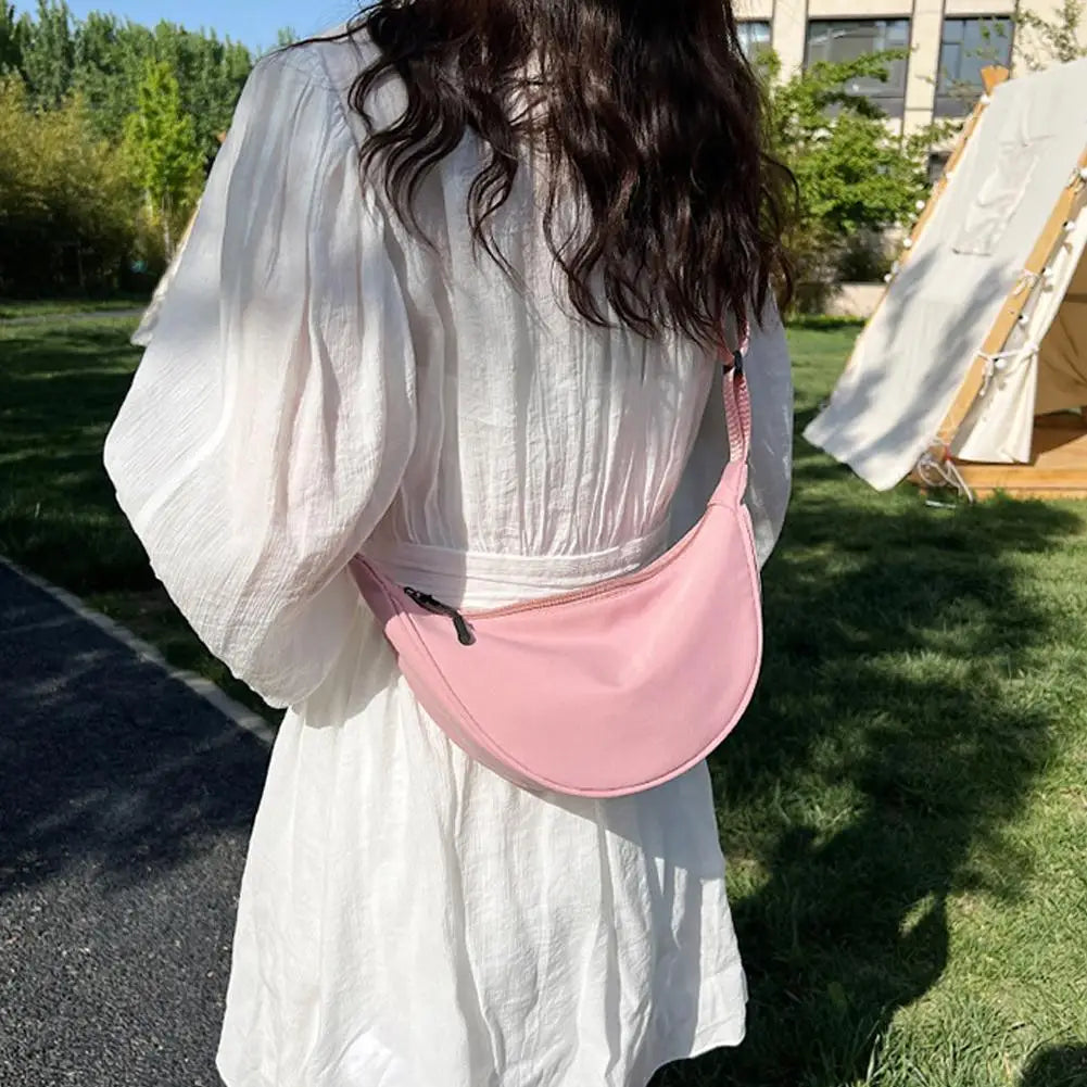 Una mujer con un vestido blanco sostiene un bolso cruz de nylon rosa en forma de media luna.
