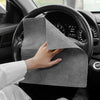 A hand is holding a gray microfiber cleaning cloth against the steering wheel of a car.
