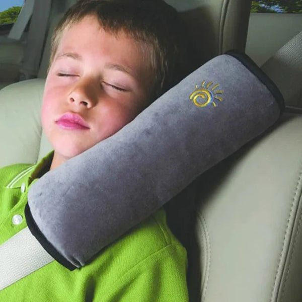 A child is resting their head on a gray shoulder comfort pillow in a car seat.