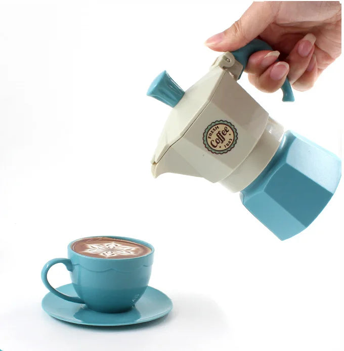 A hand is holding a light blue and cream colored coffee maker or teapot, with a matching cup and saucer visible below.