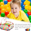 A young boy smiling while playing in a colorful ball pit with a storage basket.