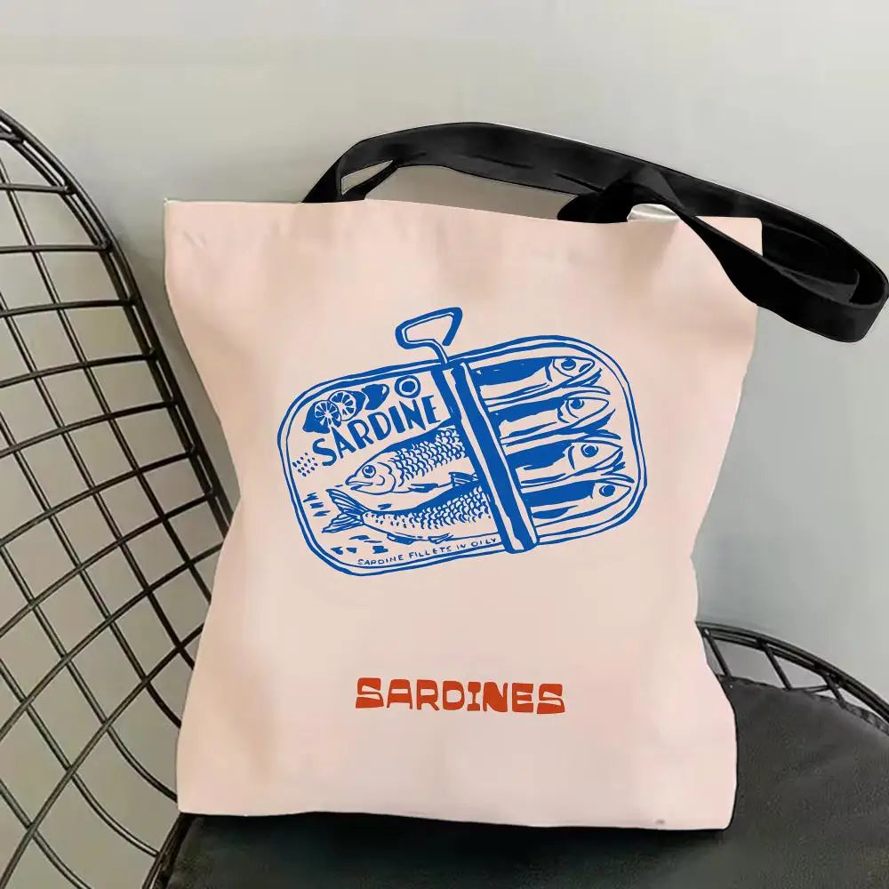 A pink canvas tote bag featuring a blue illustration of sardines and the word Sardines printed in orange.