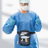 A nurse wearing a blue surgical gown and face shield holds up a black multi-pocket crossbody fanny pack.