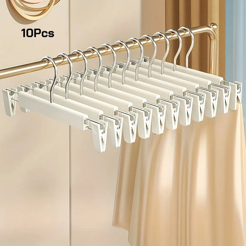A set of 10 white space-saving adjustable clip hangers for clothing displayed on a gold rod.