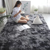 A woman sits on a dark gray Nordic furry accent rug reading a book and holding a teacup.