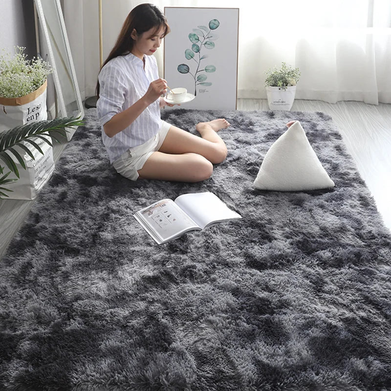 A woman sits on a dark gray Nordic furry accent rug reading a book and holding a teacup.