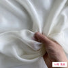 A hand is folding a piece of white silk chiffon fabric to show its drape and texture.
