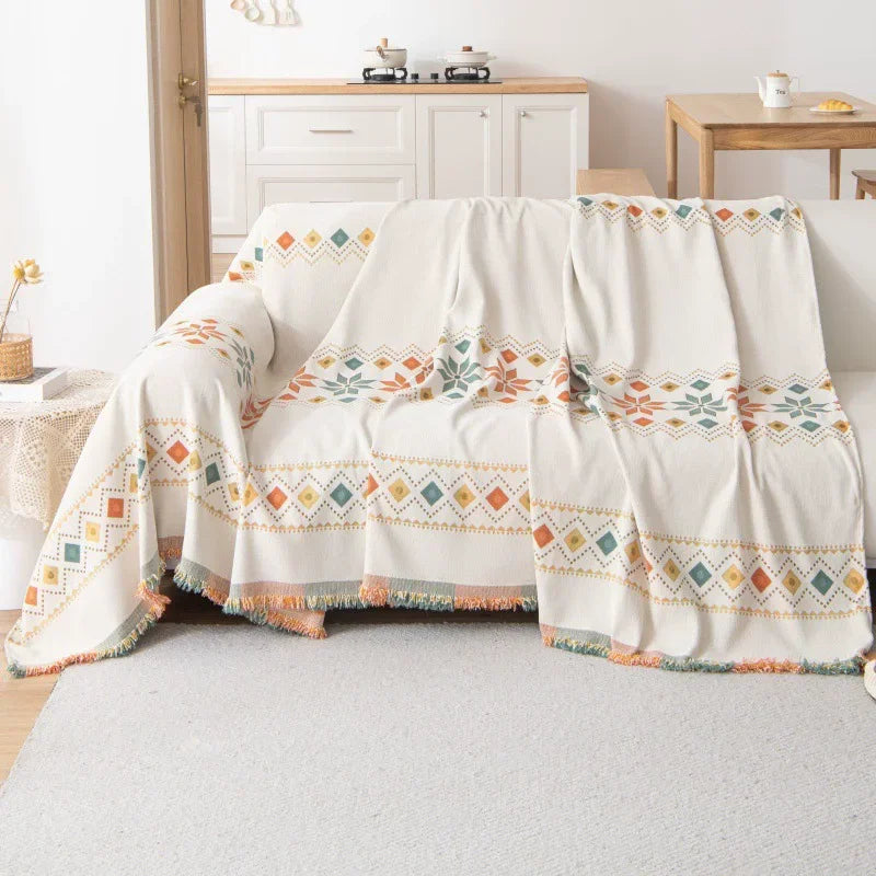 A cream and terracotta patterned bohemian jacquard sofa cover draped over a light-colored sofa.