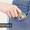 A hand is holding a small, oval-shaped bag hook with a multi-pattern design against a denim fabric background.