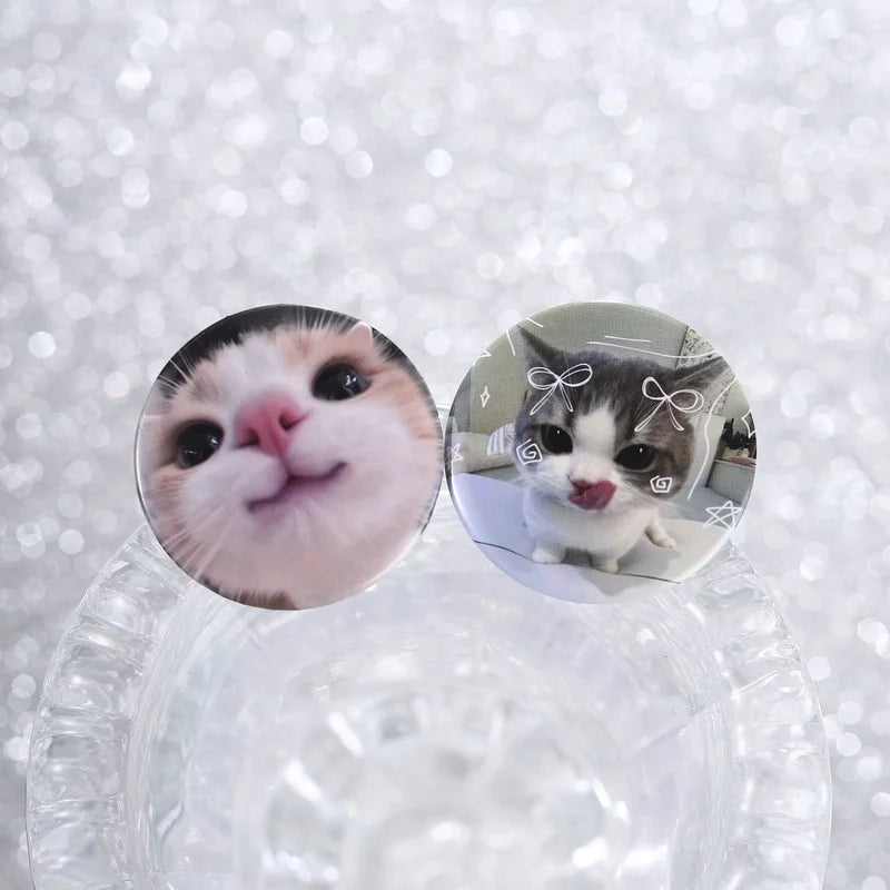 A pair of glossy tinplate pins featuring cute cat faces and expressions.