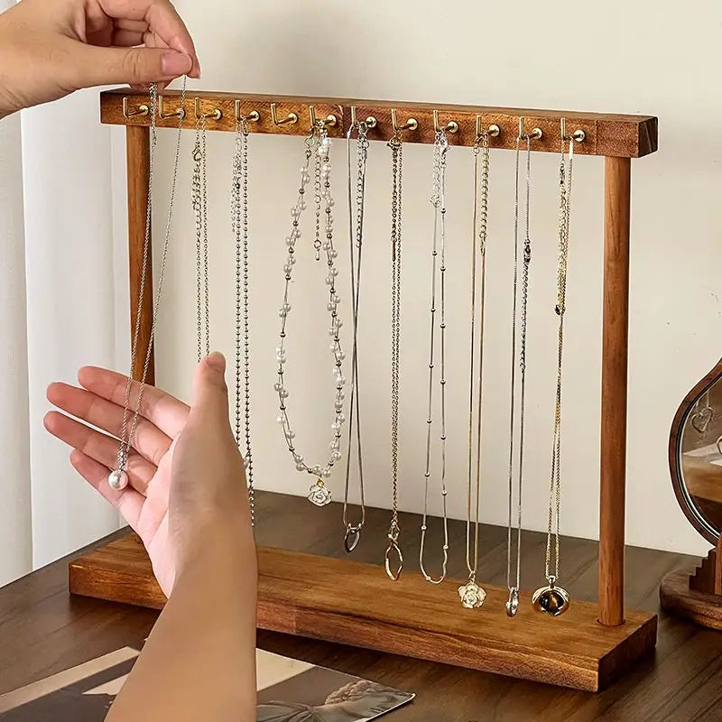 Une main accroche de délicats colliers en argent et or sur un organisateur de bijoux en bois avec des crochets.