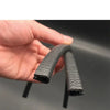 A hand holds a black U-shaped rubber edge trim with a metal core for automotive applications.