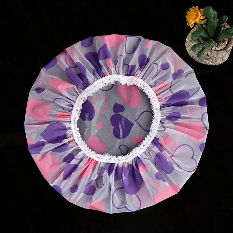 A pink and purple patterned waterproof shower cap with a white trim is shown next to a small succulent plant.