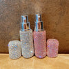 Two glass perfume atomizers, one silver and one pink, with mist spraying from the top.