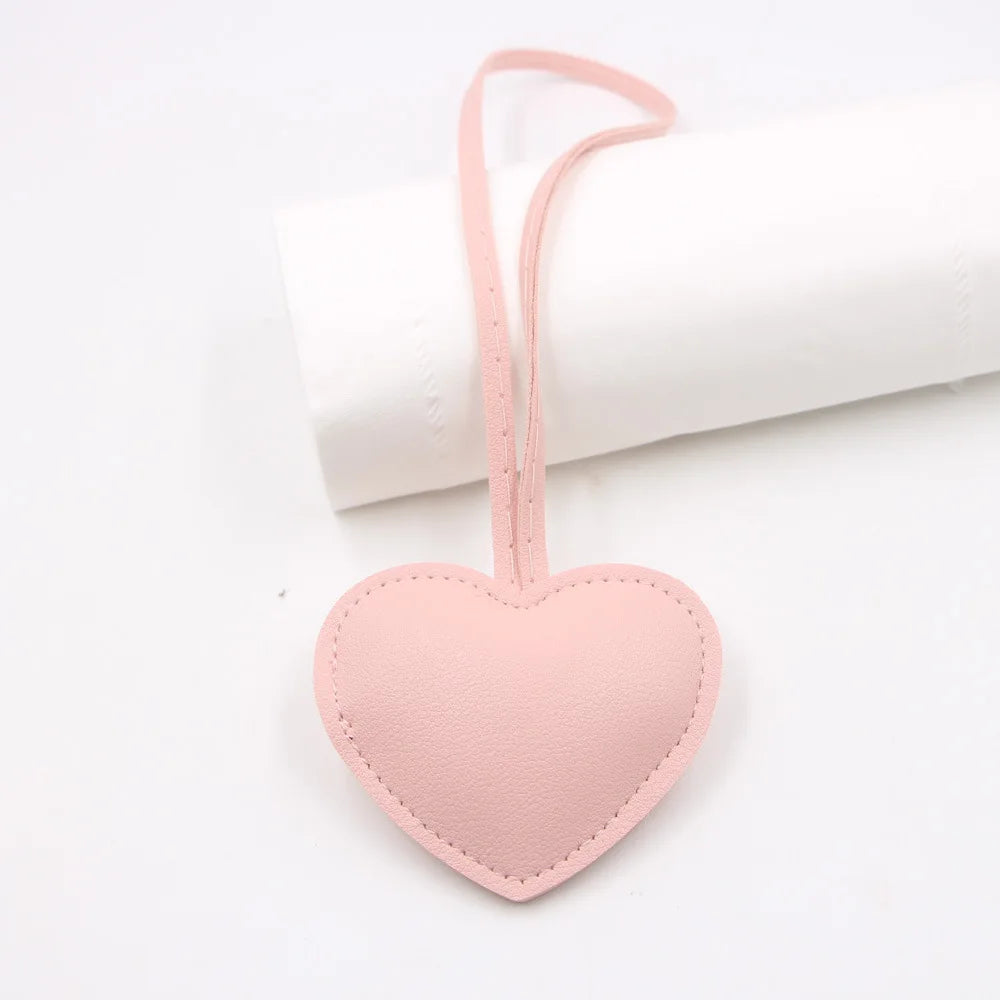 A pink heart-shaped PU leather keychain with a cotton peach charm resting on a white rolled cloth.