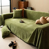 A moss green chenille sofa throw draped over a sofa, featuring decorative tassels and pillows.