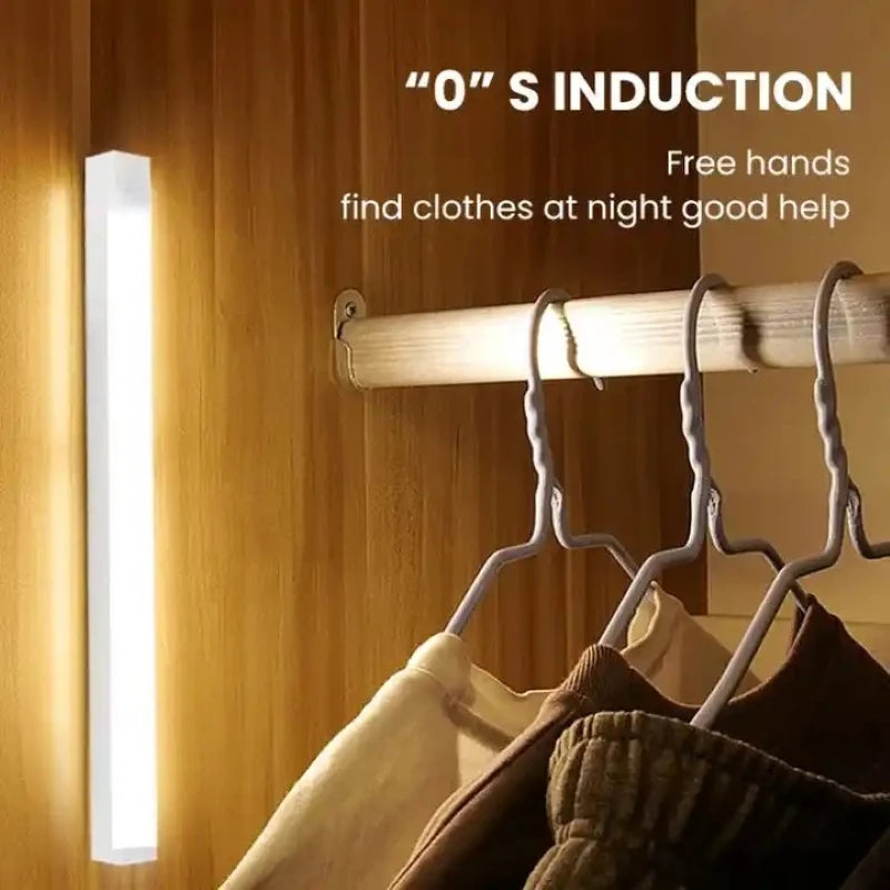 A white wireless motion-sensor night light illuminates clothes hanging on a wooden rack.