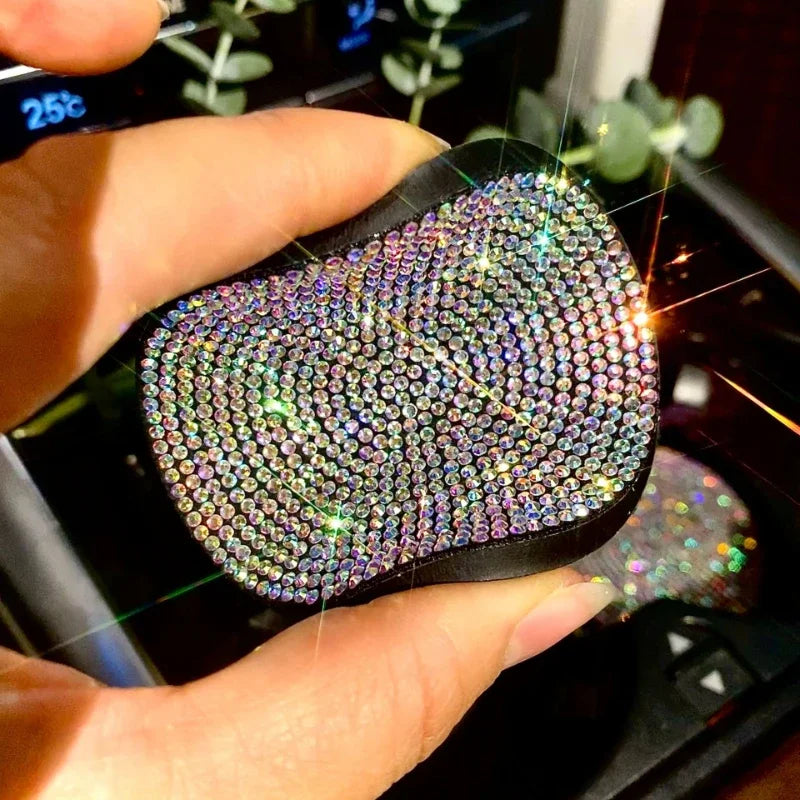 A hand holds a black, textured diamond-encrusted cup holder coaster with sparkling accents.