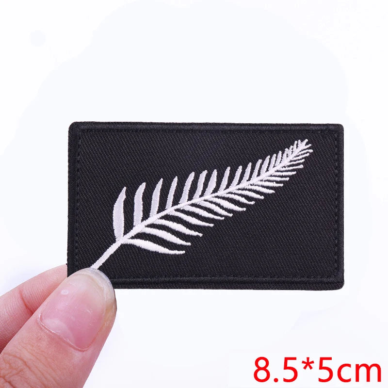 Black embroidered iron-on letter patch featuring a white fern leaf design.