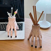 A pink resin Halloween hand planter and pen holder with a floral design sits on a wooden table next to a laptop.