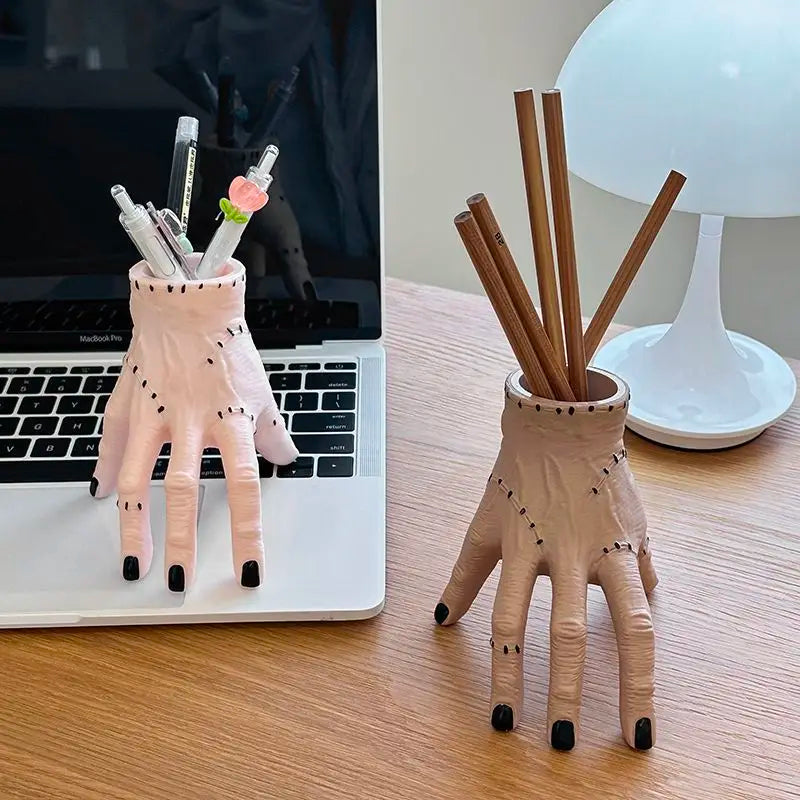 A pink resin Halloween hand planter and pen holder with a floral design sits on a wooden table next to a laptop.