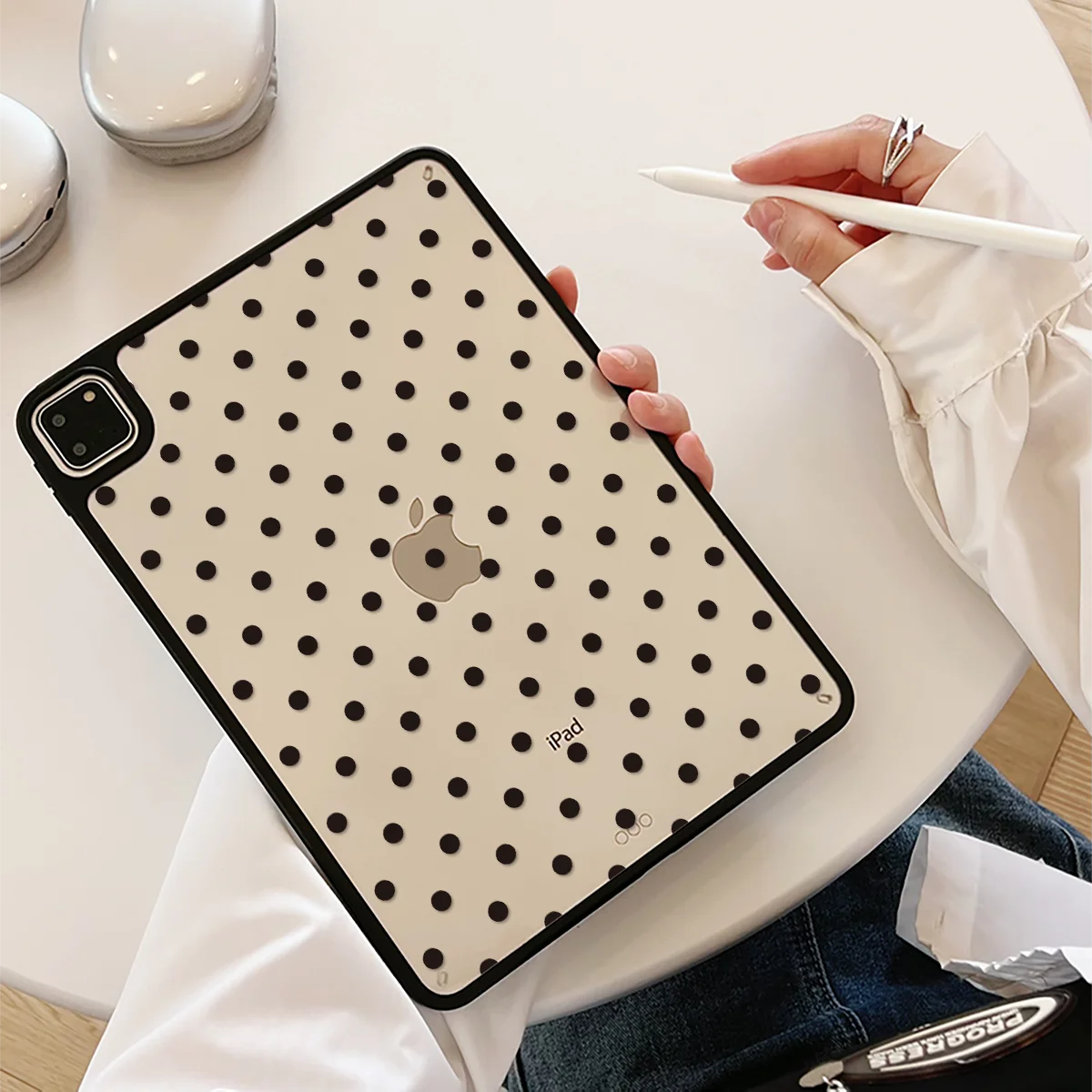 A hand holds a black polka dot protective case for an iPad on a white table.