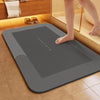 A gray non-slip bath mat is placed on a tiled floor next to a wooden cabinet and a glass shelf.