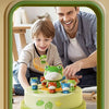 A man and a child are playing with a green jumping frog catch game on a cake.