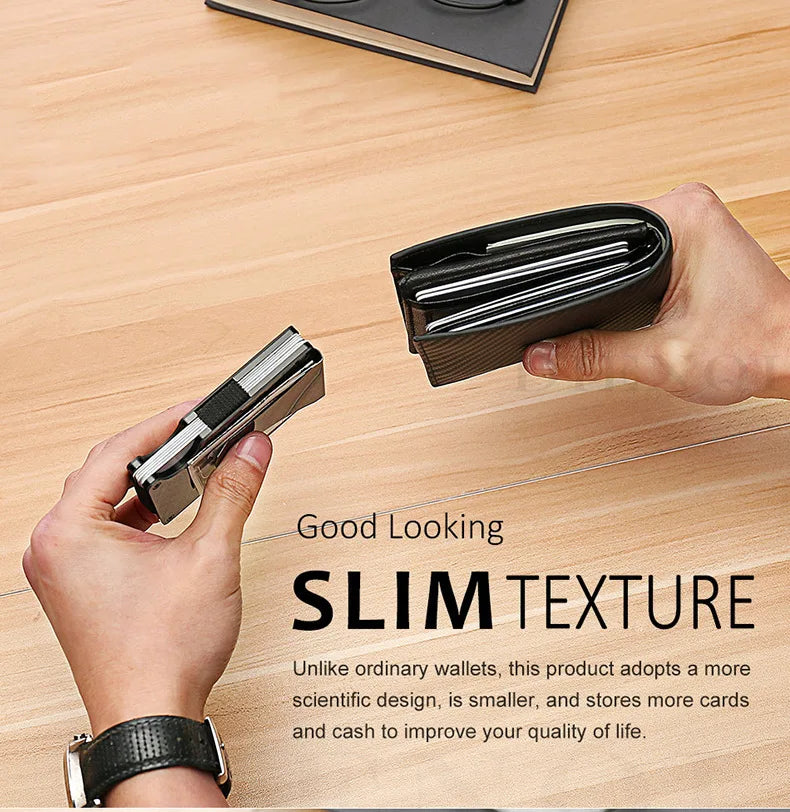 A hand holds a slim black aluminum wallet with a money clip on a wooden surface.